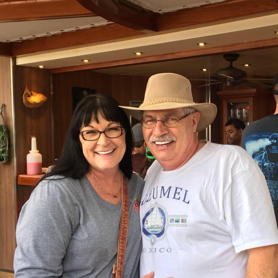 Smiling woman and man in a tan hat and Cozumel t-shirt posing together indoors.